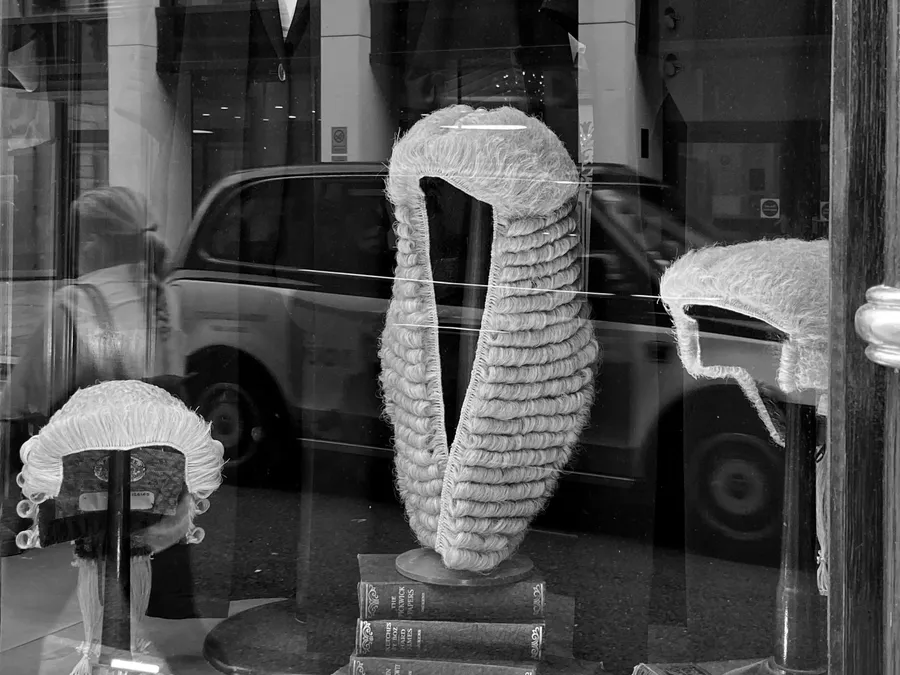 Barristers' wigs displayed in a London legal shop window, with a black cab reflected in the glass